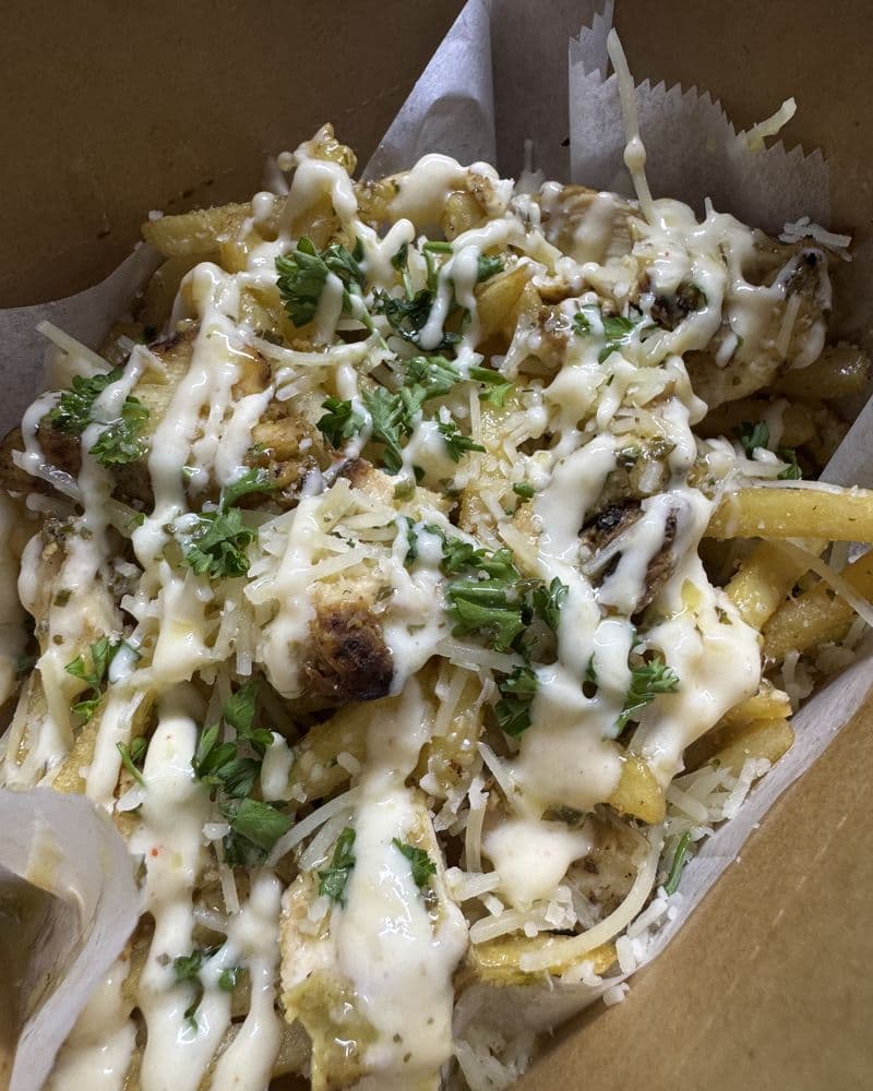 A box of fries under white sauce and herbs