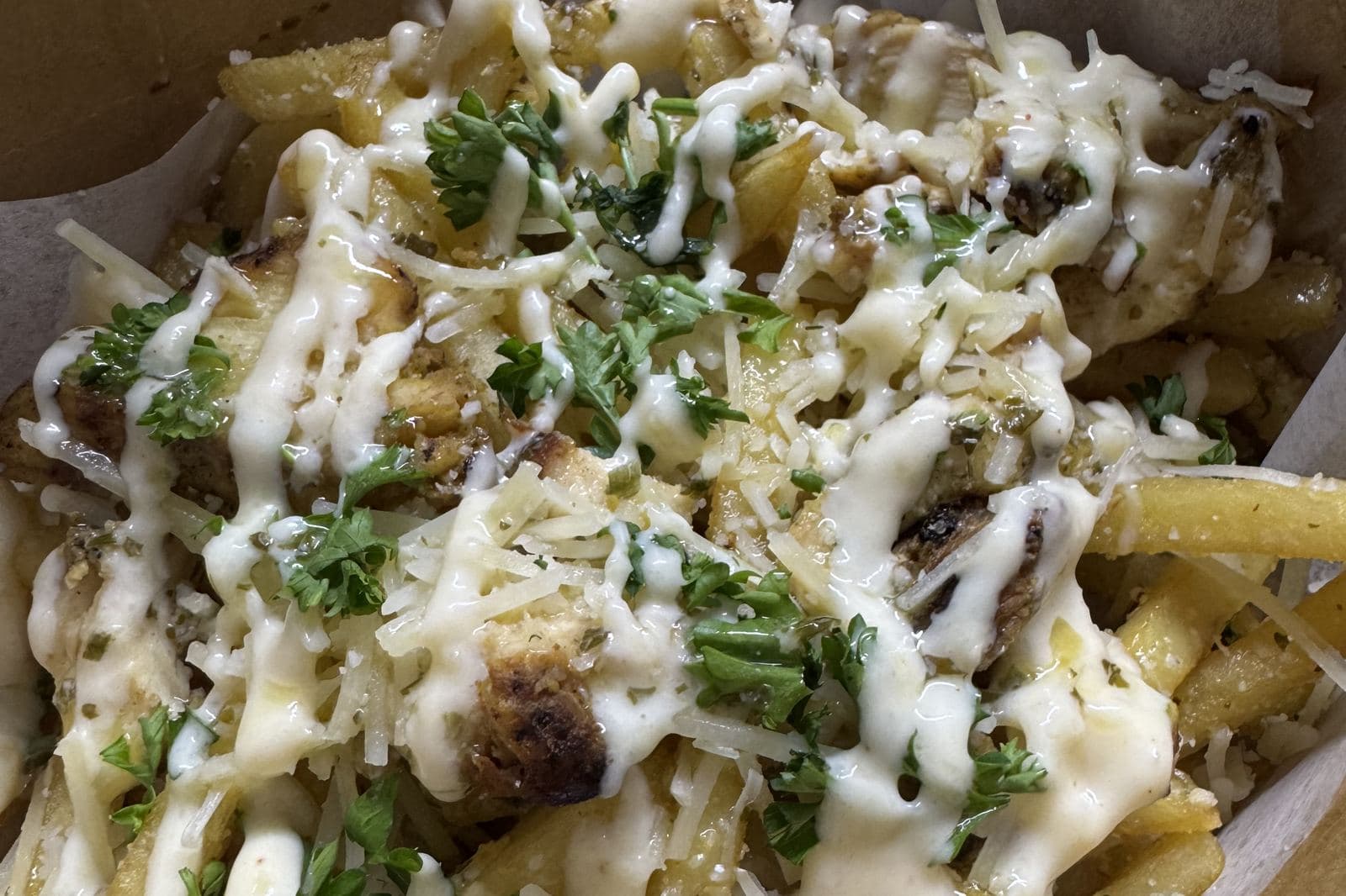 A box of fries under white sauce and herbs